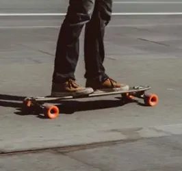 Person fährt ein Drop-Through-Longboard mit Orangatang-Rollen