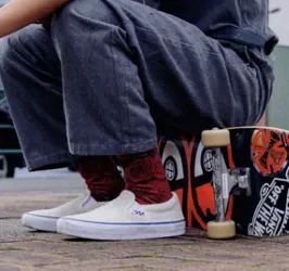 Skater zittend op een skateboard met witte skateschoenen